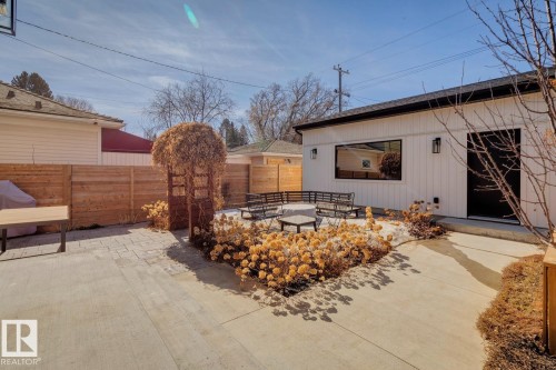 The property features a concrete patio area with integrated landscaping, a wooden privacy fence, and a modern white exterior with a black door and window trim - 11146 62 Street Nw, Edmonton, AB - Outdoor With Exterior