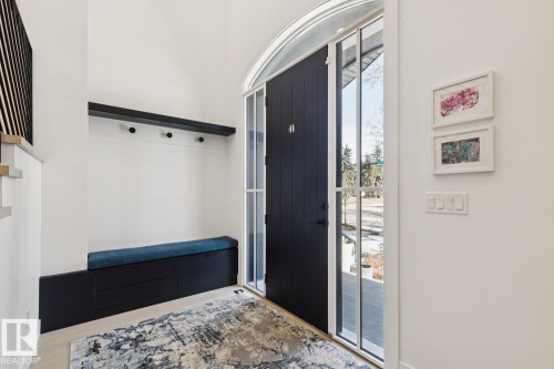 The entryway features a dark paneled door with an arched transom window, a built-in bench with storage, and a wall-mounted shelf with coat hooks - 11146 62 Street Nw, Edmonton, AB - Indoor Photo Showing Other Room