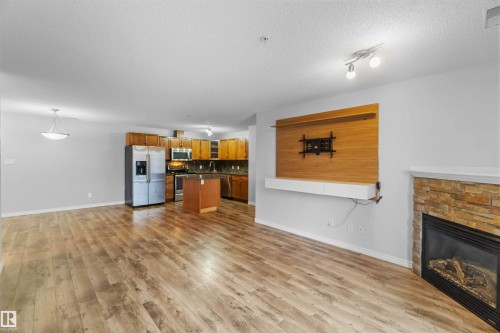 Open concept living area featuring wood-look flooring and a stone fireplace - 319 17415 99 Avenue, Edmonton, AB - Indoor Photo Showing Living Room With Fireplace