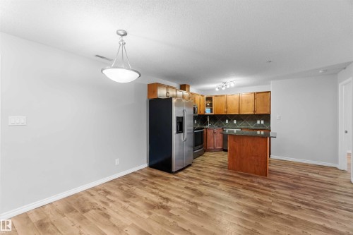This open-concept area features durable wood-look flooring and a modern ceiling light fixture - 319 17415 99 Avenue, Edmonton, AB - Indoor Photo Showing Kitchen