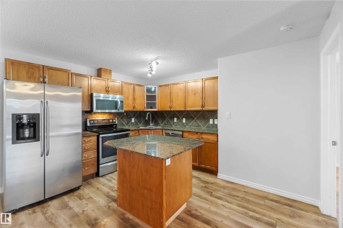 Well-appointed kitchen featuring wood cabinetry, stainless steel appliances, a tiled backsplash, and an island with a granite countertop - 319 17415 99 Avenue, Edmonton, AB - Indoor Photo Showing Kitchen With Double Sink
