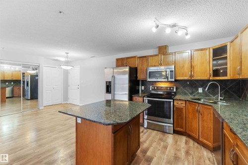 The kitchen features granite countertops, wood cabinetry, and stainless steel appliances including a refrigerator, microwave, and range - 319 17415 99 Avenue, Edmonton, AB - Indoor Photo Showing Kitchen
