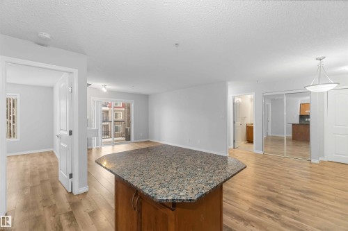 Open concept living area featuring light-toned flooring, a kitchen island with a granite countertop, and sliding glass doors leading to a balcony - 319 17415 99 Avenue, Edmonton, AB - Indoor Photo Showing Other Room