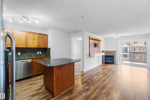 Open concept living space featuring hardwood flooring, a stone-faced fireplace, and a sliding glass door leading to a balcony - 319 17415 99 Avenue, Edmonton, AB - Indoor Photo Showing Kitchen