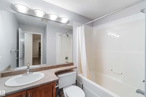 The bathroom features a vanity with a sink and countertop, a toilet, and a bathtub with a shower and shower curtain - 319 17415 99 Avenue, Edmonton, AB - Indoor Photo Showing Bathroom