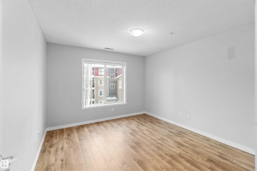 This interior space features light wood-style flooring, white walls, and a window with white trim - 319 17415 99 Avenue, Edmonton, AB - Indoor Photo Showing Other Room