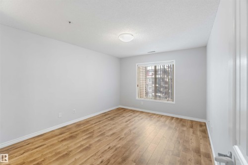 This room features light-colored walls, wood-style flooring, and a window with vertical blinds - 319 17415 99 Avenue, Edmonton, AB - Indoor Photo Showing Other Room
