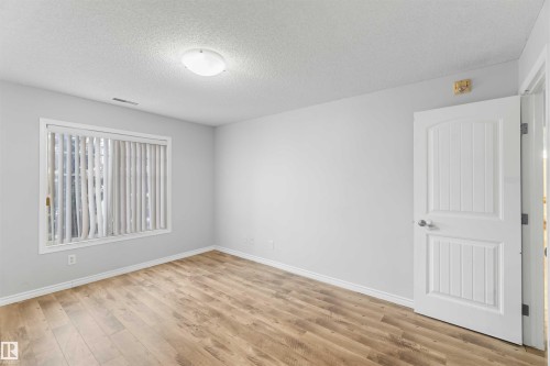 This room features light wood-look flooring, neutral wall tones, and a window with vertical blinds - 319 17415 99 Avenue, Edmonton, AB - Indoor Photo Showing Other Room