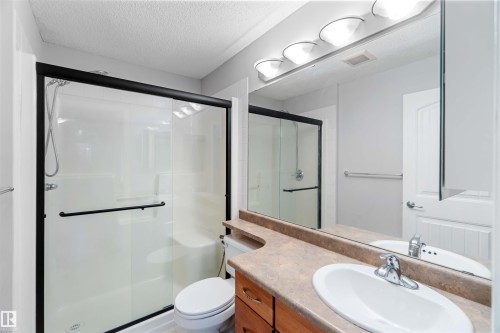 The bathroom features a shower with sliding doors and a visible shower head, a toilet, and a vanity with an integrated sink and countertop - 319 17415 99 Avenue, Edmonton, AB - Indoor Photo Showing Bathroom