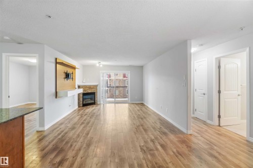 The living area features hardwood floors, a stone-faced fireplace, and a sliding glass door leading to a balcony - 319 17415 99 Avenue, Edmonton, AB - Indoor Photo Showing Other Room With Fireplace