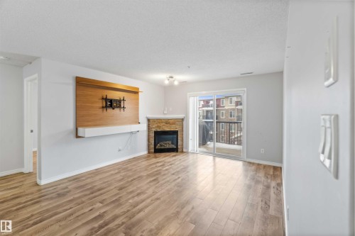 Living space featuring light wood-style flooring, a fireplace with a stone surround, and a sliding glass door leading to a balcony - 319 17415 99 Avenue, Edmonton, AB - Indoor Photo Showing Living Room With Fireplace