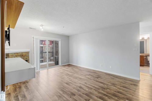 Living area featuring light wood flooring, light grey walls, and a stone-clad fireplace - 319 17415 99 Avenue, Edmonton, AB - Indoor Photo Showing Other Room
