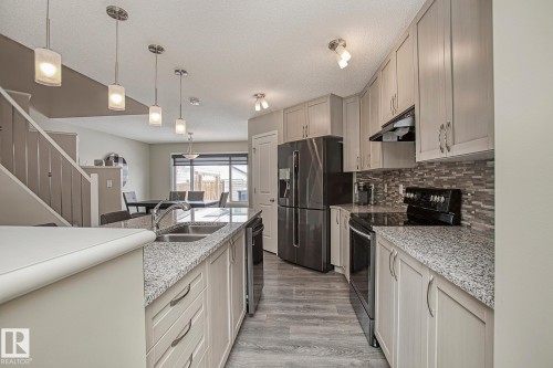 The kitchen features light-toned cabinetry, granite countertops, and stainless steel appliances - 7718 Eifert Crescent, Edmonton, AB - Indoor Photo Showing Kitchen With Double Sink With Upgraded Kitchen