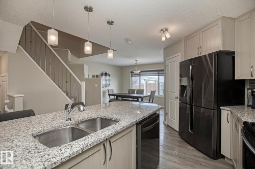 The kitchen features a double basin stainless steel sink set within a granite countertop, light-colored cabinetry, and a black refrigerator - 7718 Eifert Crescent, Edmonton, AB - Indoor Photo Showing Kitchen With Double Sink