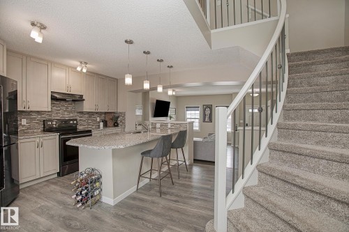 The property features a kitchen with light-colored cabinetry, a textured tile backsplash, dark appliances, and a granite-topped island with pendant lighting - 7718 Eifert Crescent, Edmonton, AB - Indoor Photo Showing Kitchen With Upgraded Kitchen