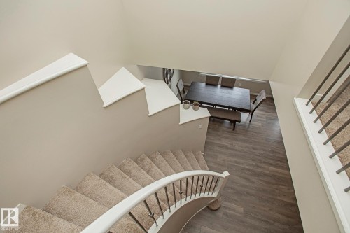 The property features a curved staircase with carpeted treads and a white banister with dark balusters, overlooking a dining area with wood-look flooring - 7718 Eifert Crescent, Edmonton, AB - Indoor Photo Showing Other Room