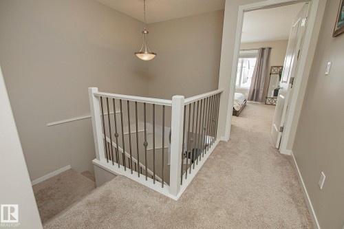 The property features a staircase with carpeted treads and a white newel post and balustrade with metal spindles - 7718 Eifert Crescent, Edmonton, AB - Indoor Photo Showing Other Room