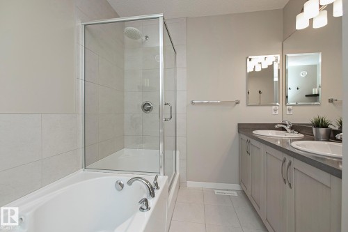 The bathroom features a combination tub and shower with a glass enclosure, dual vanity sinks with chrome fixtures, and tiled flooring - 7718 Eifert Crescent, Edmonton, AB - Indoor Photo Showing Bathroom