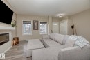 This bright living area features wood-look flooring, an electric fireplace with a white mantle, and two windows providing natural light - 7718 Eifert Crescent, Edmonton, AB  - Indoor Photo Showing Living Room With Fireplace 