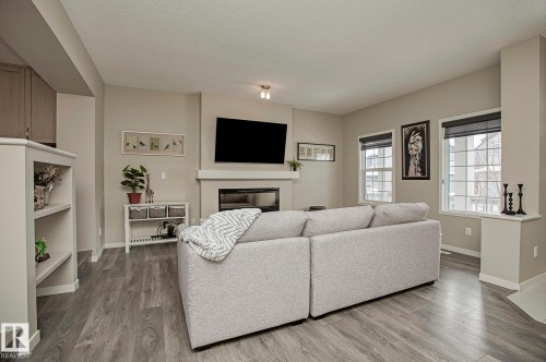 Living room featuring light-colored walls, wood-look flooring, a fireplace, and multiple windows - 7718 Eifert Crescent, Edmonton, AB - Indoor Photo Showing Living Room With Fireplace