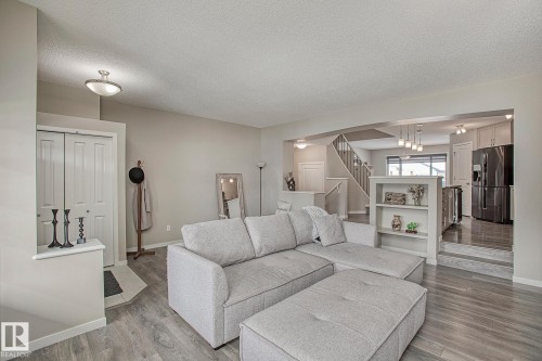 The living area features light-toned flooring, a light-colored sectional, and a built-in shelving unit - 7718 Eifert Crescent, Edmonton, AB - Indoor Photo Showing Living Room