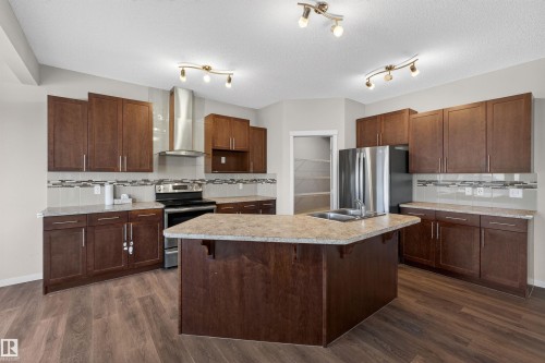 The kitchen features dark wood cabinetry, granite-style countertops, and a central island with a double sink - 4723 Alwood Bend, Edmonton, AB - Indoor Photo Showing Kitchen With Stainless Steel Kitchen With Double Sink With Upgraded Kitchen