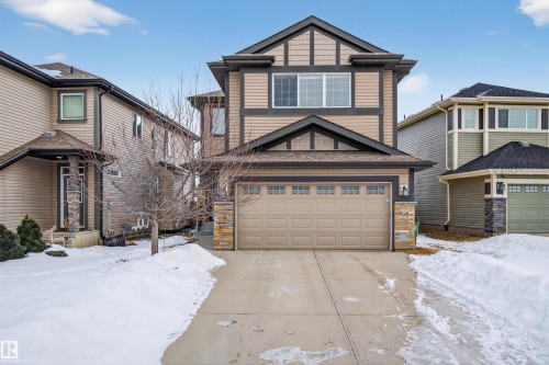 This property features a two-story exterior with light brown siding, dark brown trim, and a prominent front-facing garage - 4723 Alwood Bend, Edmonton, AB - Outdoor With Facade