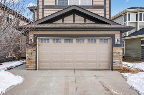 The property features a double garage with a paneled door and window inserts, accented by stone veneer columns - 4723 Alwood Bend, Edmonton, AB - Outdoor