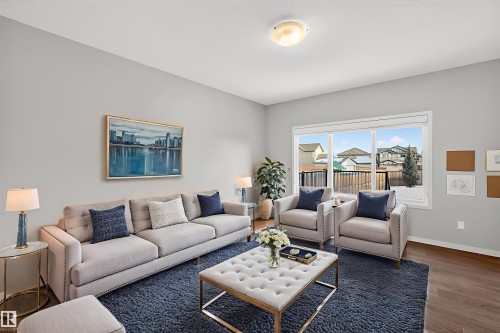 Living area featuring hardwood flooring, light grey walls, and a large window providing views of the surrounding homes and a tree - 4723 Alwood Bend, Edmonton, AB - Indoor Photo Showing Living Room
