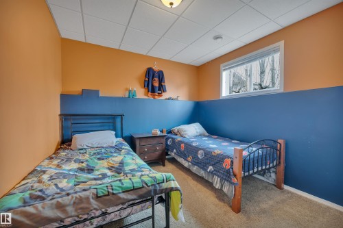 This room features a window providing natural light, a neutral carpeted floor, and walls painted in a two-tone scheme of orange and blue - 5 Parkview Crescent, Calmar, AB - Indoor Photo Showing Bedroom