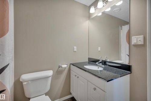 The bathroom features a white vanity with a dark granite countertop, a white toilet, and a large wall mirror with overhead lighting - 5 Parkview Crescent, Calmar, AB - Indoor Photo Showing Bathroom