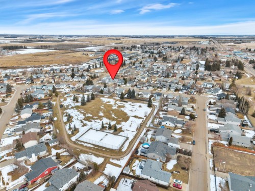 Aerial view of the property's setting within a residential area, featuring surrounding homes with various roof styles and a nearby undeveloped lot with some trees and visible patches of snow - 5 Parkview Crescent, Calmar, AB - Outdoor With View