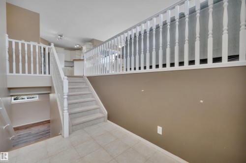 A well-lit interior featuring a carpeted staircase with white railings, leading down to a lower level with wood-style flooring and a small window - 5 Parkview Crescent, Calmar, AB - Indoor Photo Showing Other Room