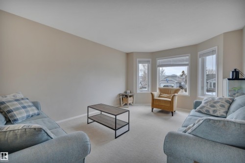 This room features light-colored carpeting, neutral painted walls, and a large bay window providing ample natural light - 5 Parkview Crescent, Calmar, AB - Indoor Photo Showing Living Room