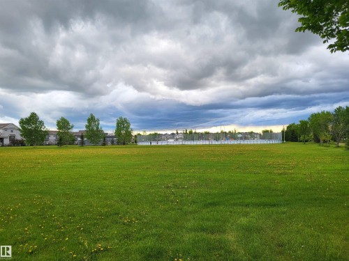 Expansive green space with distant residential buildings and trees under a dramatic sky - 32 2121 Haddow Drive, Edmonton, AB - Outdoor With View