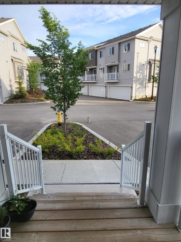 Exterior view featuring wooden steps, white railings, and a concrete pathway leading to a landscaped area with a tree - 32 2121 Haddow Drive, Edmonton, AB - Outdoor With Deck Patio Veranda With Exterior