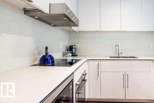 Modern kitchen featuring white cabinetry, light-colored countertops, a stainless steel range hood, and a stainless steel sink with a chrome faucet - 2506 10360 102 Street, Edmonton, AB - Indoor Photo Showing Kitchen With Double Sink With Upgraded Kitchen