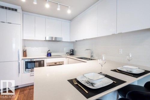 The kitchen features white cabinetry, integrated appliances, a stainless steel range hood, a tiled backsplash, and an island with a countertop sink - 2506 10360 102 Street, Edmonton, AB - Indoor Photo Showing Kitchen With Double Sink With Upgraded Kitchen