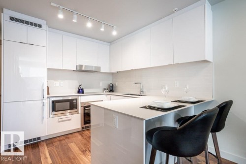 The kitchen features bright white cabinetry, stainless steel appliances, a white backsplash, and a breakfast bar - 2506 10360 102 Street, Edmonton, AB - Indoor Photo Showing Kitchen With Upgraded Kitchen