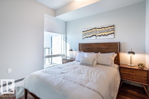 This bedroom features hardwood floors, a large window with a roller shade, and a wood headboard - 2506 10360 102 Street, Edmonton, AB - Indoor Photo Showing Bedroom