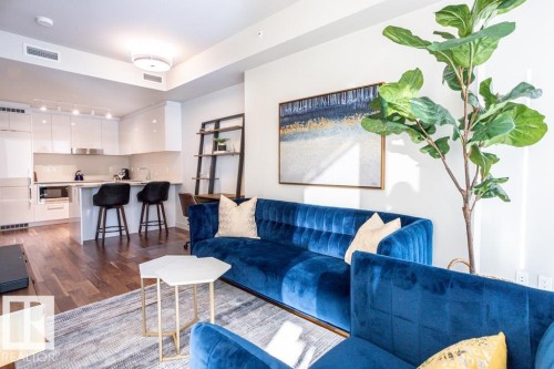 Open concept living space featuring hardwood floors, a kitchen with white cabinetry and stainless steel appliances, and a central island with seating - 2506 10360 102 Street, Edmonton, AB - Indoor Photo Showing Living Room