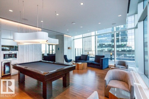 This expansive common area features hardwood flooring, a modern pool table, and full-height windows offering views of nearby buildings - 2506 10360 102 Street, Edmonton, AB - Indoor Photo Showing Other Room