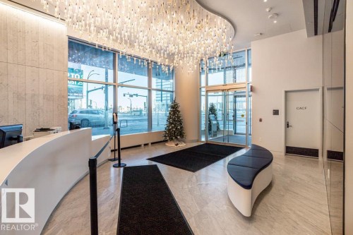 Lobby featuring a curved reception desk, large windows providing natural light, and a modern chandelier - 2506 10360 102 Street, Edmonton, AB - Indoor Photo Showing Other Room