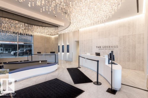 The property features a reception area with a large, curved desk, a prominent wall sign, and a decorative ceiling light fixture - 2506 10360 102 Street, Edmonton, AB - Indoor