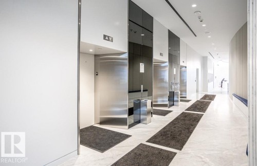The building features a hallway with light-colored marble flooring, recessed lighting, and multiple elevators with brushed metal doors - 2506 10360 102 Street, Edmonton, AB - Indoor Photo Showing Other Room