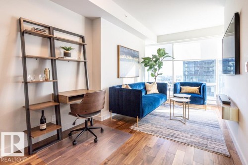 Living area featuring hardwood flooring, a wall-mounted shelving unit with a desk, and large windows with cityscape views - 2506 10360 102 Street, Edmonton, AB - Indoor