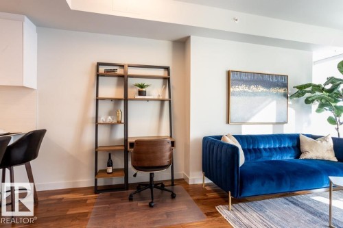 Living area featuring hardwood flooring, a modern blue sofa, and a wall-mounted shelving unit - 2506 10360 102 Street, Edmonton, AB - Indoor
