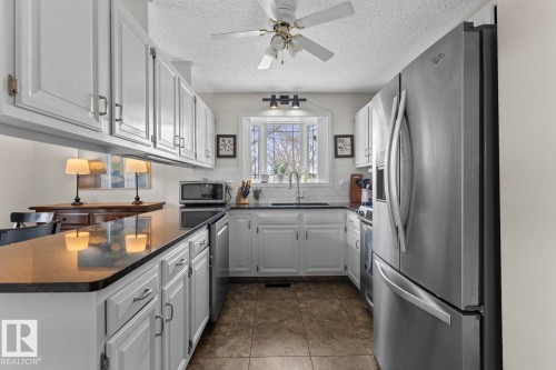 The kitchen features white cabinetry, dark countertops, and stainless steel appliances - 4003 50A Avenue, Cold Lake, AB - Indoor Photo Showing Kitchen With Stainless Steel Kitchen
