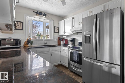 The kitchen features white cabinetry, a bay window with natural light, subway tile backsplash, and stainless steel appliances including a refrigerator and range - 4003 50A Avenue, Cold Lake, AB - Indoor Photo Showing Kitchen With Stainless Steel Kitchen