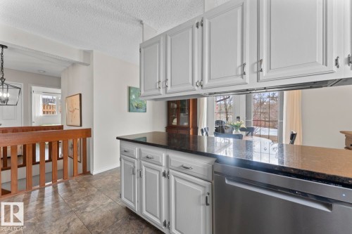 The kitchen features white cabinetry with silver hardware, a dark countertop, and a stainless steel dishwasher - 4003 50A Avenue, Cold Lake, AB - Indoor Photo Showing Other Room
